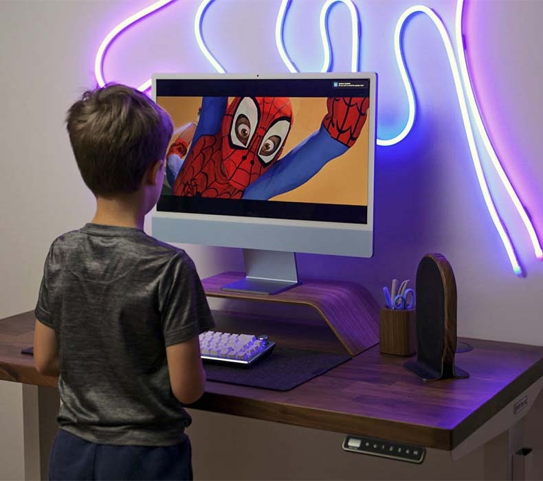 A young boy enters the Spiderverse on his computer at his Walnut Solid Wood UPLIFT Standing Desk