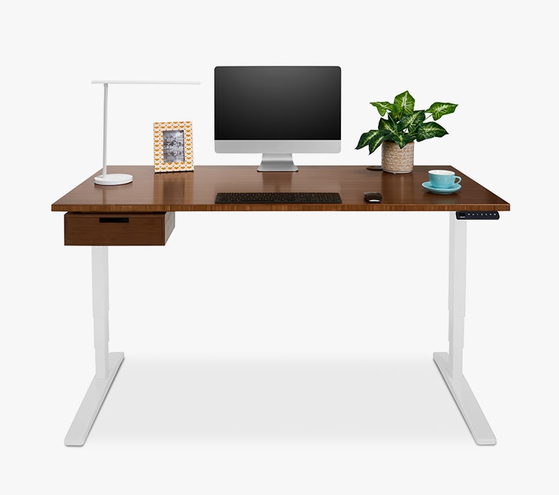 The best standing desk, pictured with a dark bamboo desktop and drawer, white frame, and desk accessories