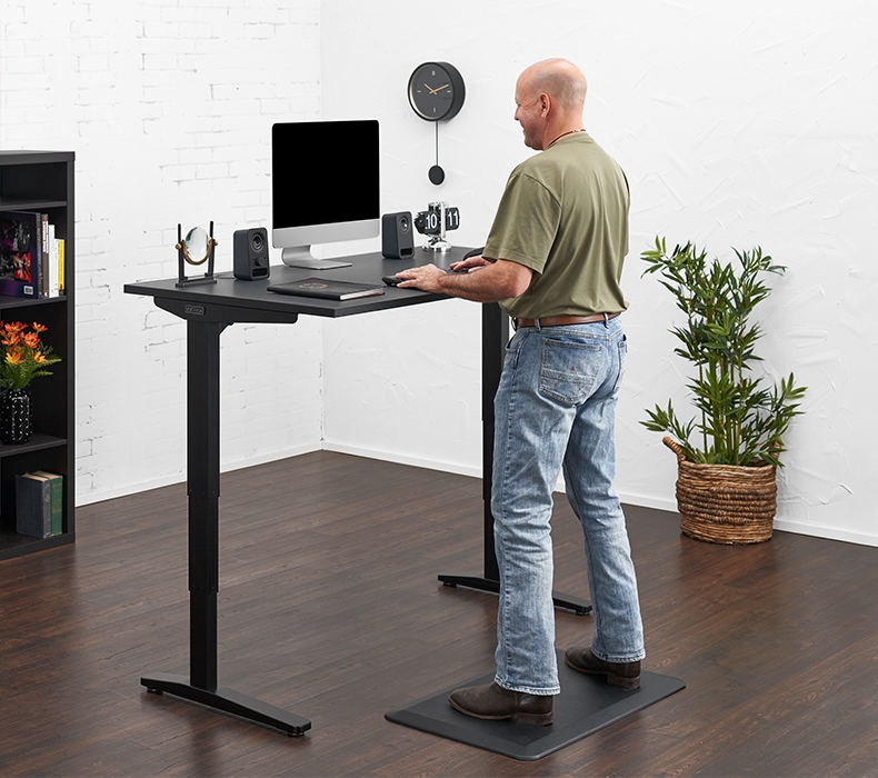 A person standing at a 60" x 30" Black Laminate UPLIFT Standing Desk on an anti-fatigue Standing Desk Mat