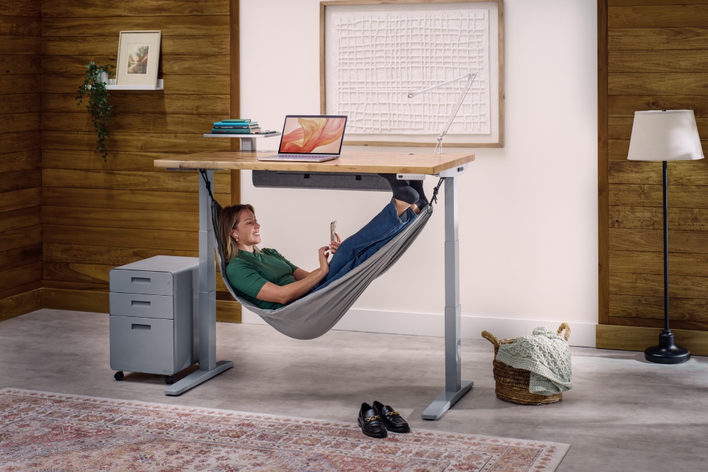 Person sitting in an Under Desk Hammock attached to the Uplift Standing Desk using included Anchor Plates.