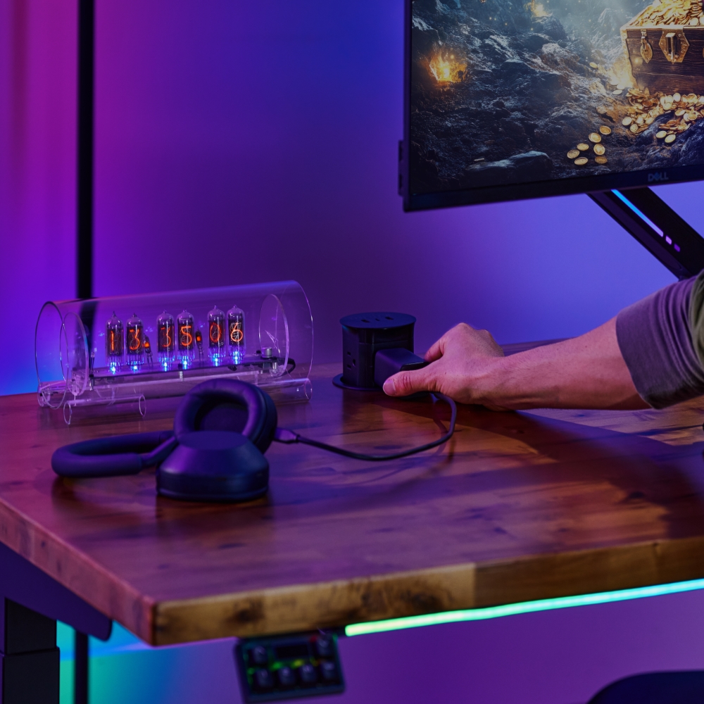 Gamer plugging into UPLIFT Desk Pop Up Power Grommet for convenient gaming power.