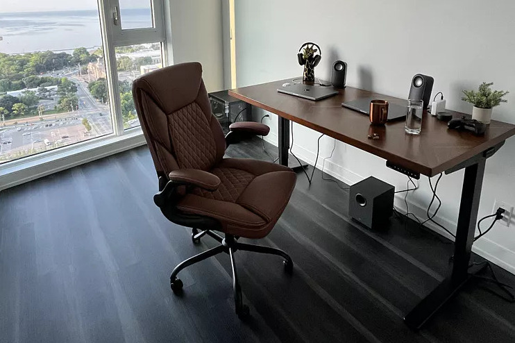 A home office with an Uplift Standing Desk, a brown leather chair, and a large window overlooking a city and a lake.