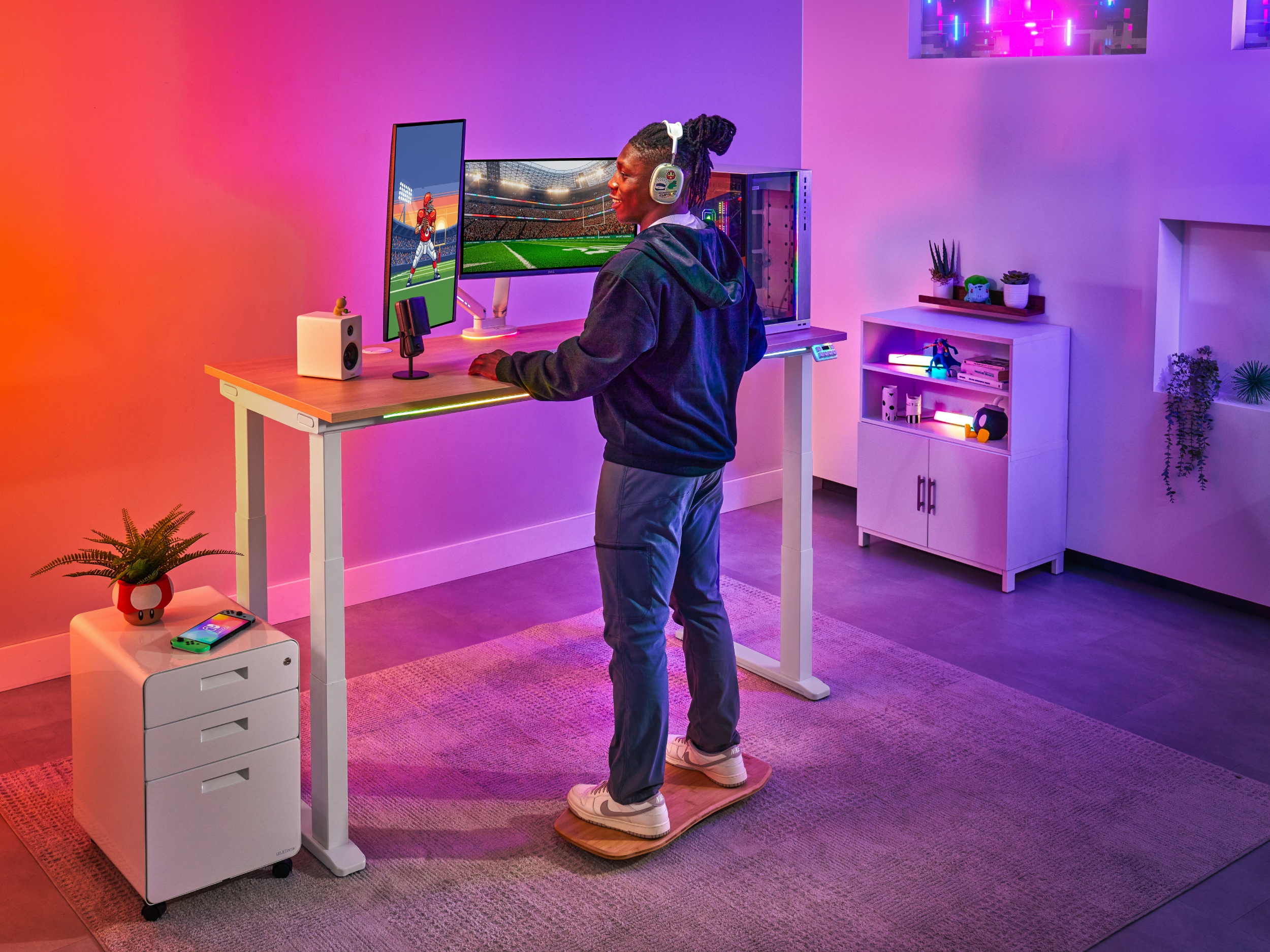 Man standing on top of a motion board at a V3 4-leg standing desk playing video games next to a filing cabinet and mopac cabinet