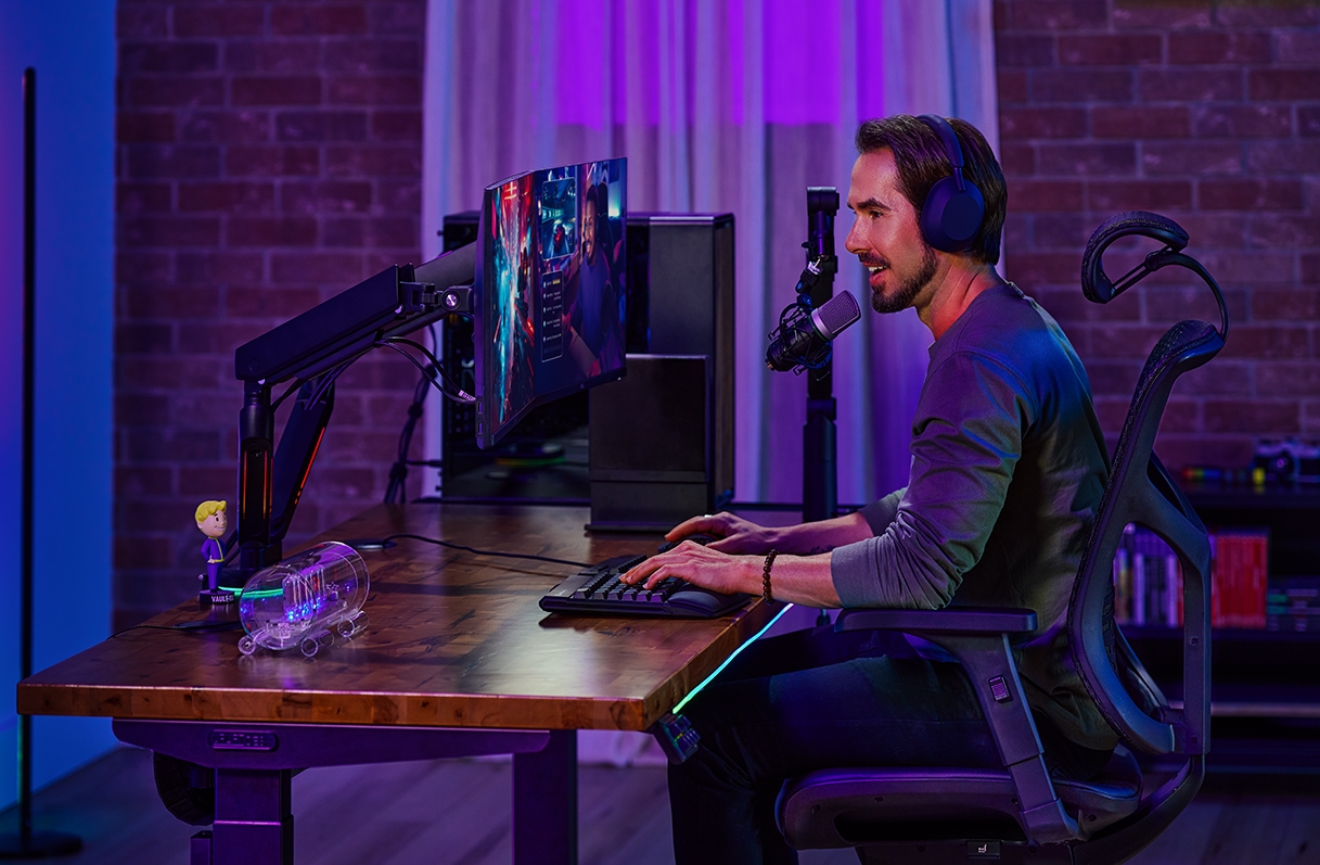 Person sitting and speaking into a microphone at an Uplift Standing Desk in Black with a Saman Butcher Block Desktop.