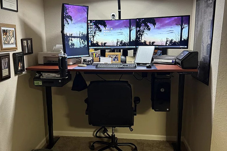 A modern office space featuring an Uplift Standing Desk with a multi-monitor setup, a black office chair, and framed decor.
