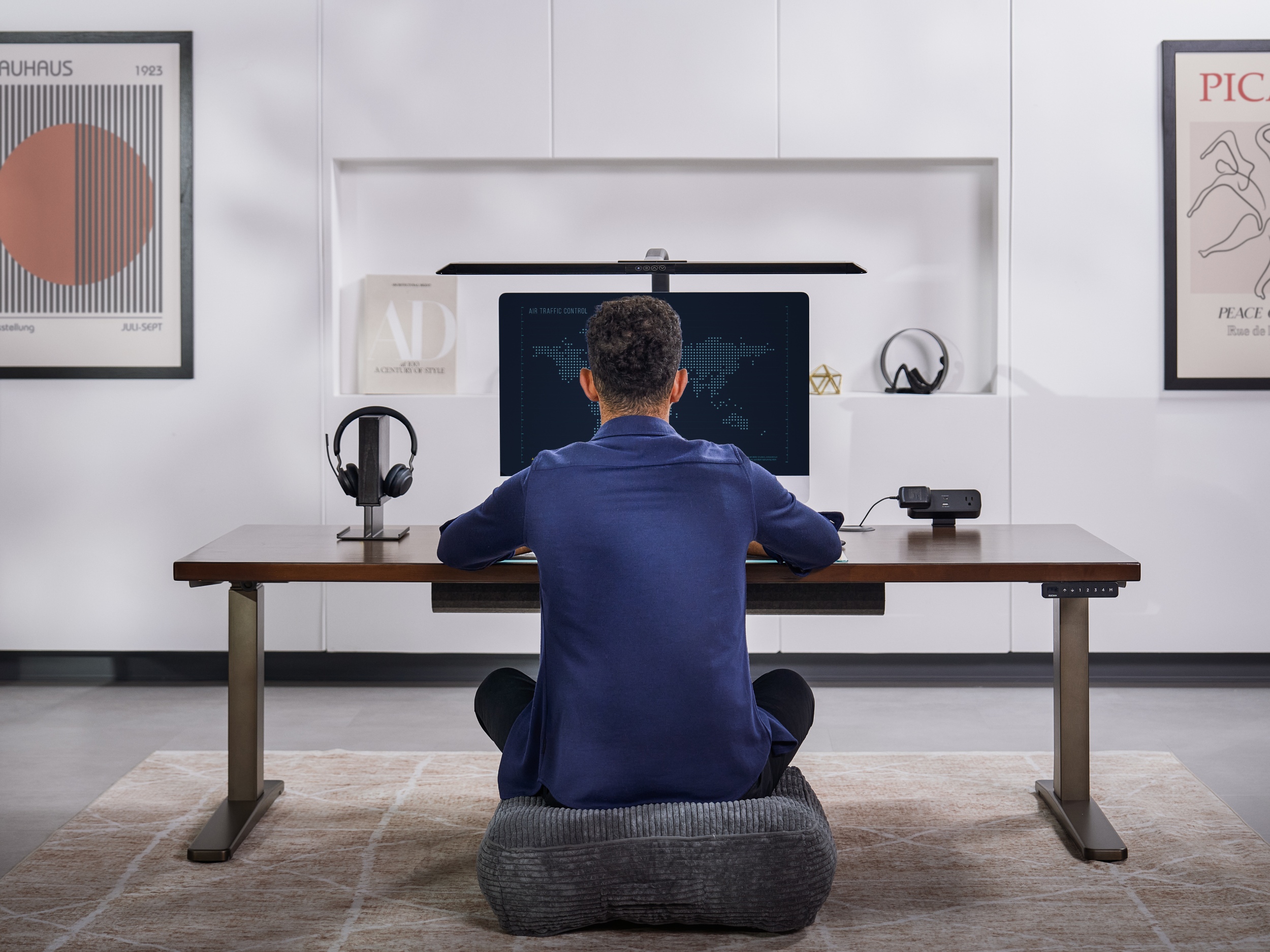 Man sitting on cushion at a V3 2-leg standing desk at the lowest height