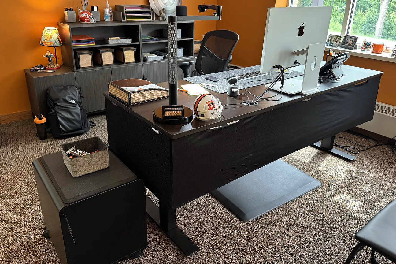 An office with bright orange walls and hobby decor featuring an Uplift Standing Desk with Privacy Panels in the center of the room.
