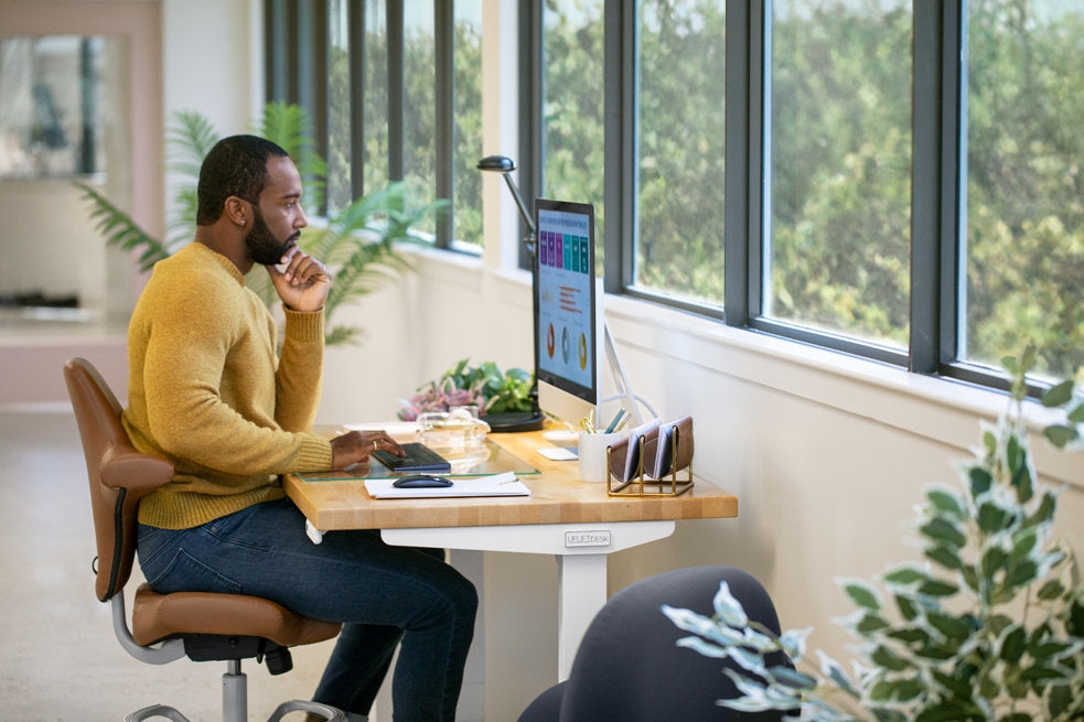 Person looking inquisitive while sitting on a Capisco chair at an UPLIFT Height Adjustable desk.