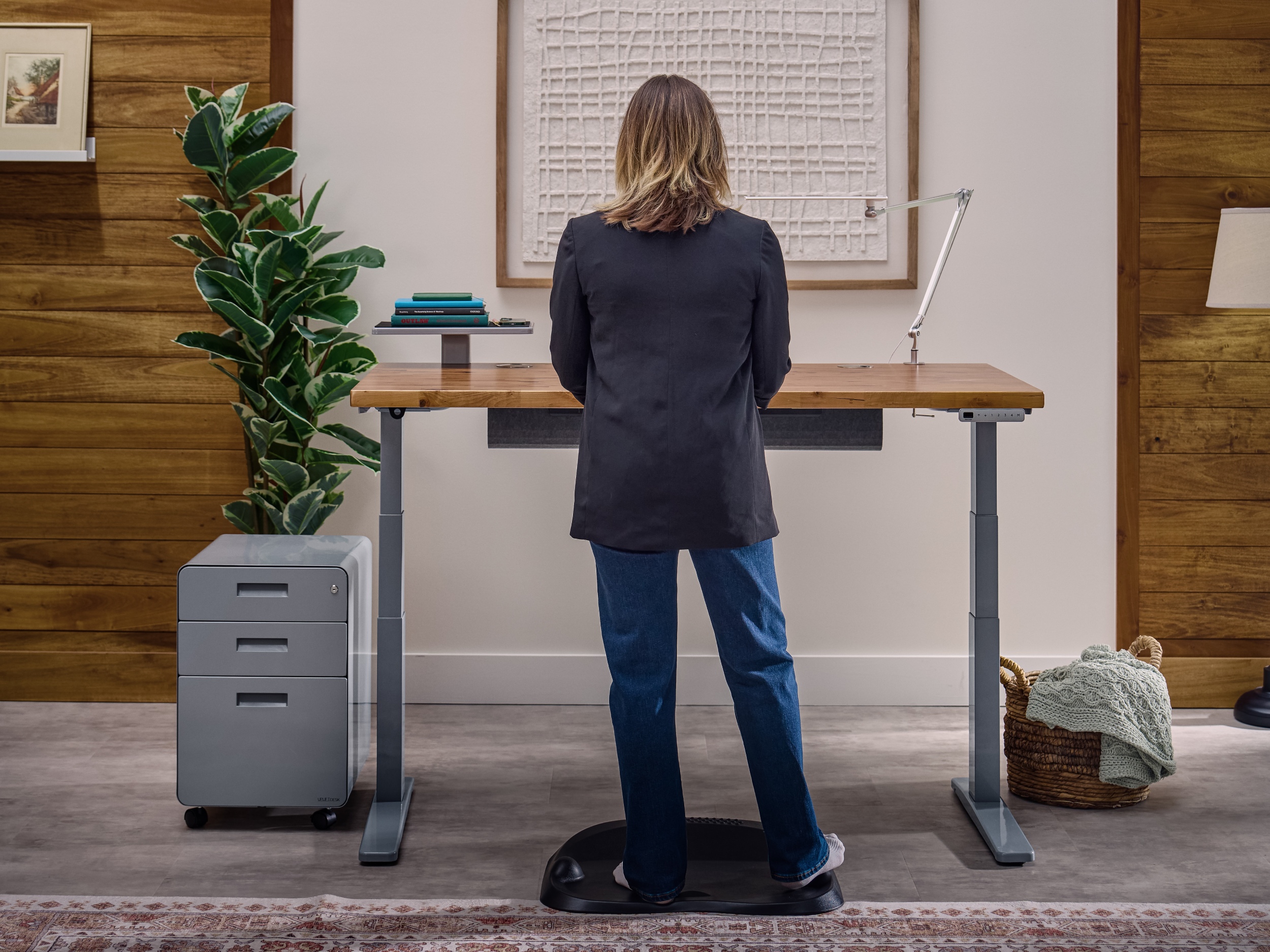 Woman standing on mat at a V3 2-leg standing desk next to a filing cabinet