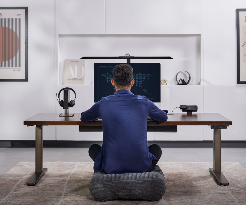Person sitting on floor cushion working at an Uplift Standing Desk at its lowest height.