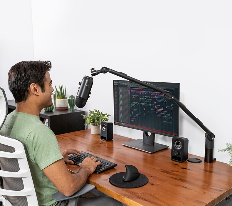 A person working at an UPLIFT Desk speaking into a microphone supported by a Clamp-On Microphone Arm