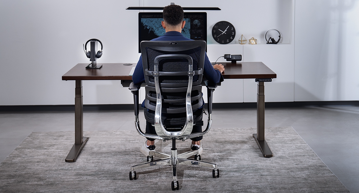 Person sitting in an Intuition Ergonomic Chair at an Uplift Standing Desk.