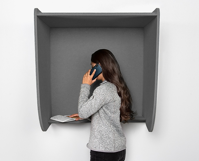 A person takes a call in an Acoustic Wall-Mounted Phone Booth