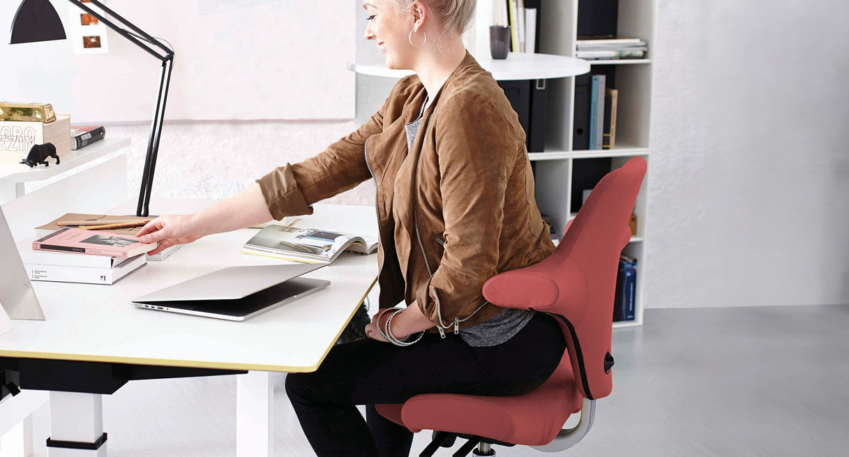 A person in an ergonomic HAG Capisco Chair working at her desk