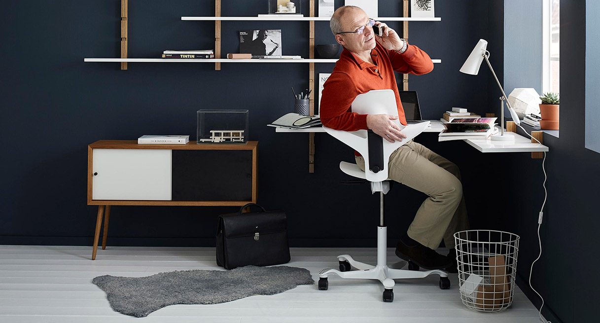 A person taking a phone call at their desk while seated in a HAG Capisco Puls Chair