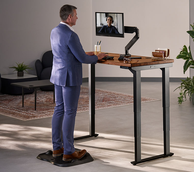 Professional at an UPLIFT 4-leg Standing Desk with ergonomic setup including a monitor arm and anti-fatigue mat
