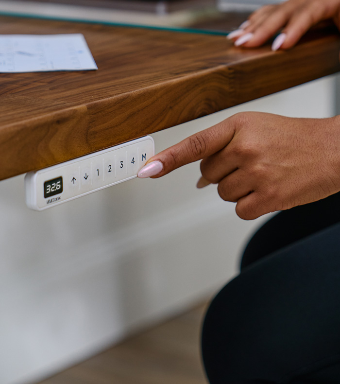 Person pressing a button on the Advanced Keypad attached to an Uplift Standing Desk.