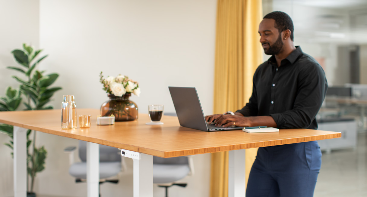 Man standing at an UPLIFT Height Adjustable 42" bamboo Conference Table while working on laptop.