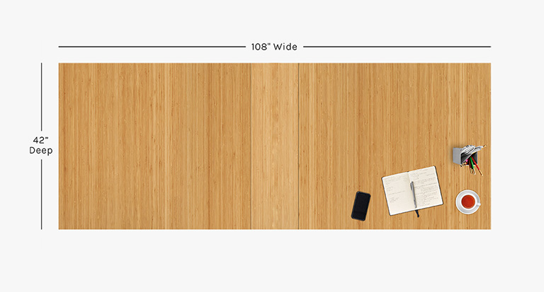 Overhead view of 108" x 42" Bamboo Tabletop with center leaf and black power grommets, plus various desk items.